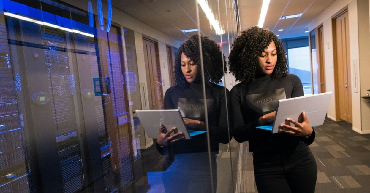 an IT director leaning against a wall while using a surface laptop